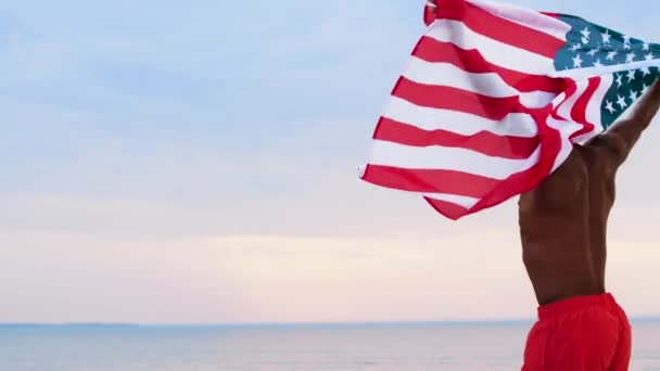 Szczęśliwy człowiek Afryki z amerykańską flagę na plaży — Wideo stockowe
