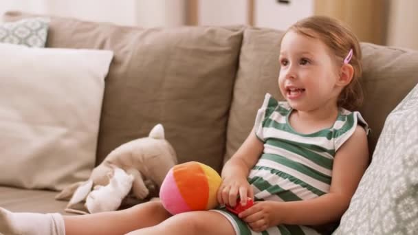 Счастливая девочка, сидящая на диване с игрушками дома — стоковое видео