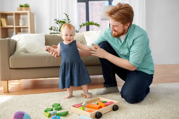 Bebé niña de pie con padre ayuda en casa — Foto de Stock