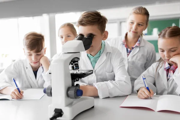 Niños o estudiantes con biología de microscopio en la escuela — Foto de Stock