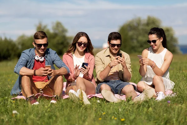 Amigos sonrientes con teléfonos inteligentes sentados en la hierba — Foto de Stock