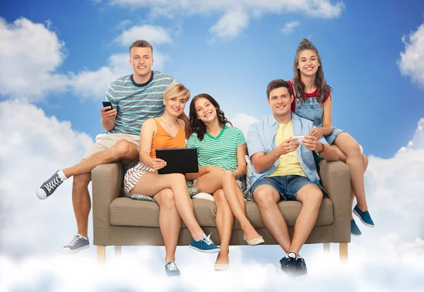 Друзья с планшетным ПК и смартфоны сидеть на диване — стоковое фото