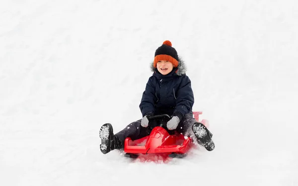 Felice ragazzo scorrevole sulla slitta giù collina di neve in inverno — Foto Stock