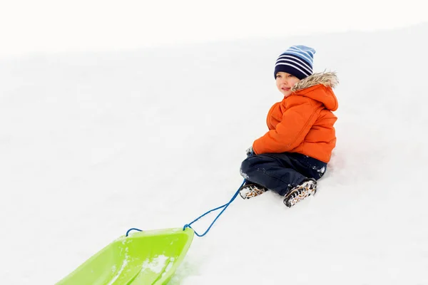 Menino feliz com trenó na colina de neve no inverno — Fotografia de Stock