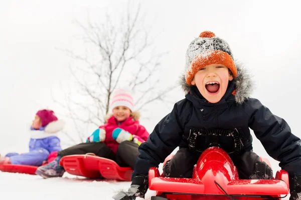 Niños felices deslizándose en trineos en invierno — Foto de Stock