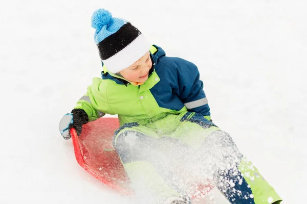 Menino feliz deslizando no trenó colina de neve no inverno — Fotografia de Stock