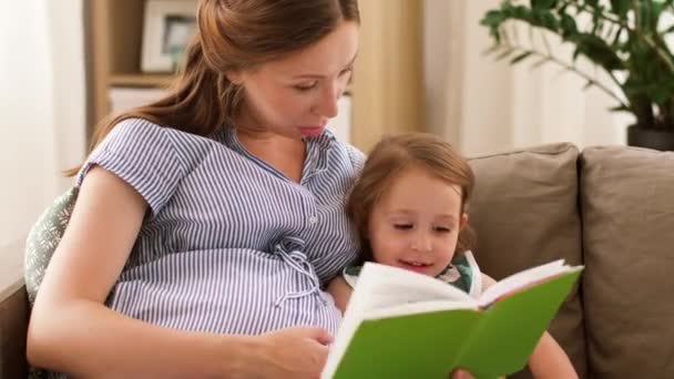 Pregnant mother and daughter reading book at home — Stock Video