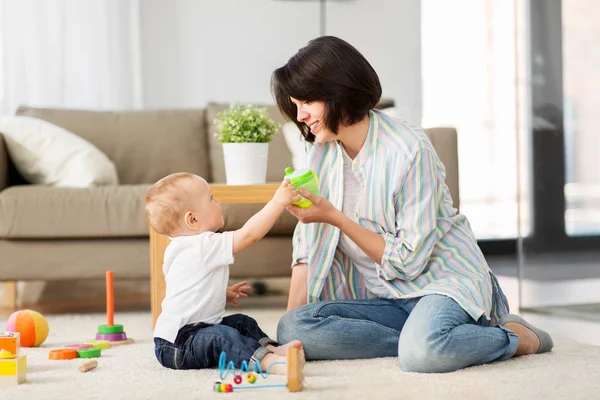 Feliz madre dando sippy taza a bebé hijo en casa —  Fotos de Stock