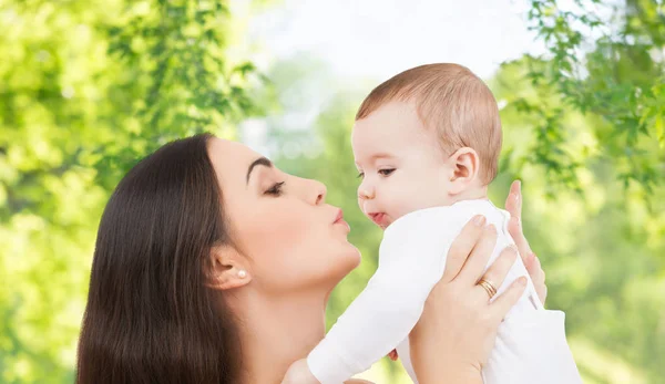 Mãe beijando bebê sobre fundo natural verde — Fotografia de Stock