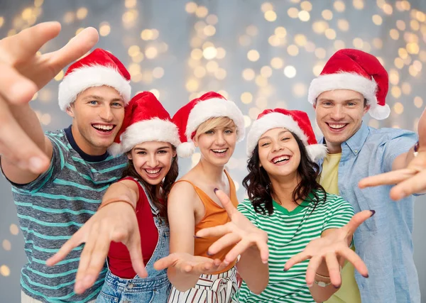 Happy vrienden in santa hoeden over feestelijke verlichting — Stockfoto