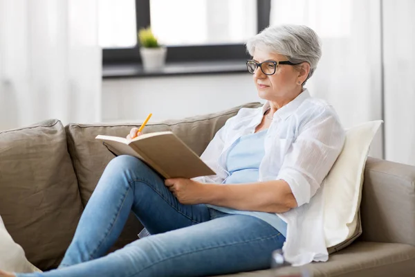 Wanita senior menulis ke notebook atau buku harian di rumah — Stok Foto