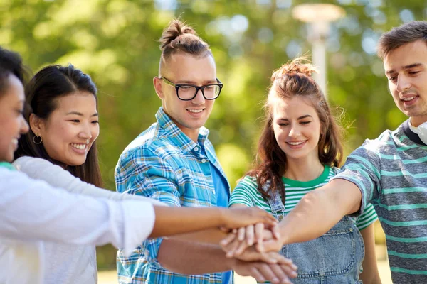 Felice sorridente amici accatastamento mani nel parco — Foto Stock