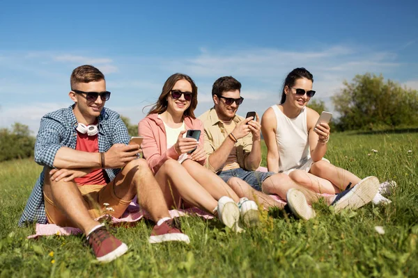 Lachende vrienden met smartphones zitten op gras — Stockfoto