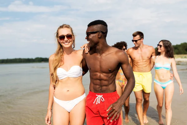 Pareja de raza mixta caminando a lo largo de la playa con amigos — Foto de Stock