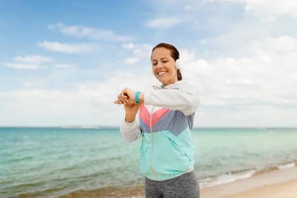Femme avec écouteurs et fitness tracker sur la plage — Photo