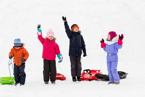 Niños felices con trineos agitando las manos en invierno —  Fotos de Stock