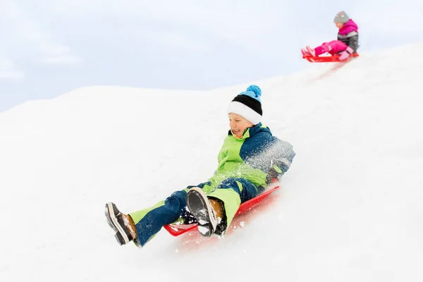Счастливые дети катаются на санках вниз по холму зимой — стоковое фото