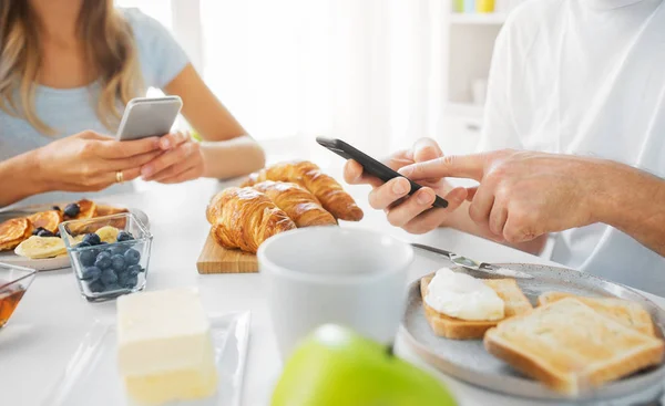 Close up of couple with smartphones at breakfast — Stock Photo, Image