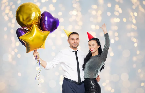 Glückliches Paar in Party-Hüten mit Luftballons — Stockfoto