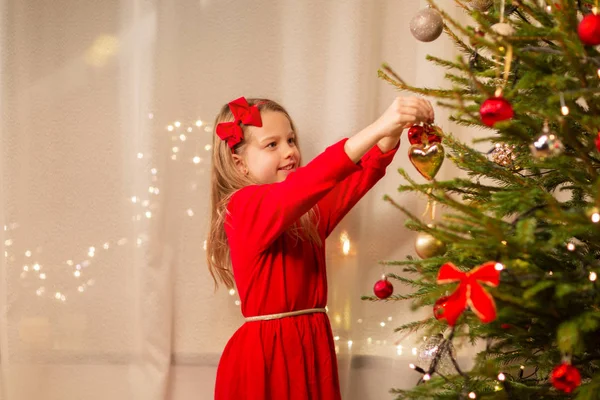 Chica feliz en vestido rojo decorando árbol de Navidad — Foto de Stock