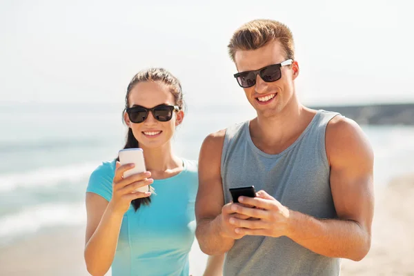 Couple en vêtements de sport avec smartphones sur la plage — Photo