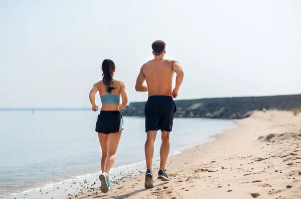 Casal em roupas esportivas correndo ao longo da praia — Fotografia de Stock