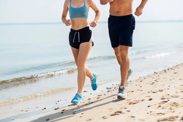 Coppia in abiti sportivi che corre lungo sulla spiaggia — Foto Stock