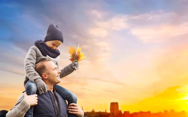 Vater trägt Sohn mit Herbstlaub in die Stadt — Stockfoto
