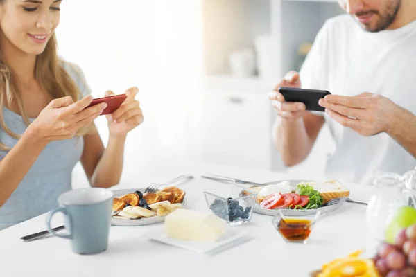 Close up of couple with smartphones at breakfast — Stock Photo, Image