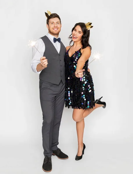 Casal feliz com coroas e sparklers na festa — Fotografia de Stock