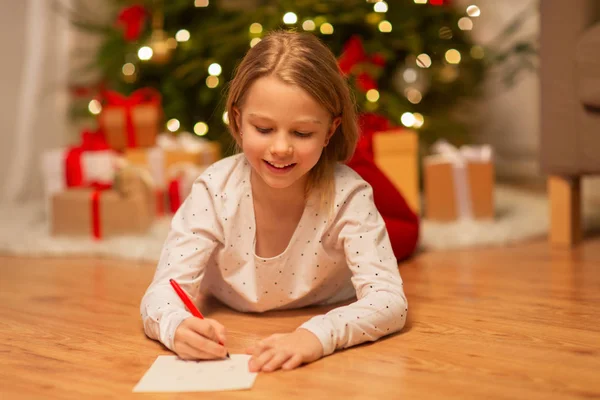 Smiling girl writing christmas wish list at home — Stock Photo, Image