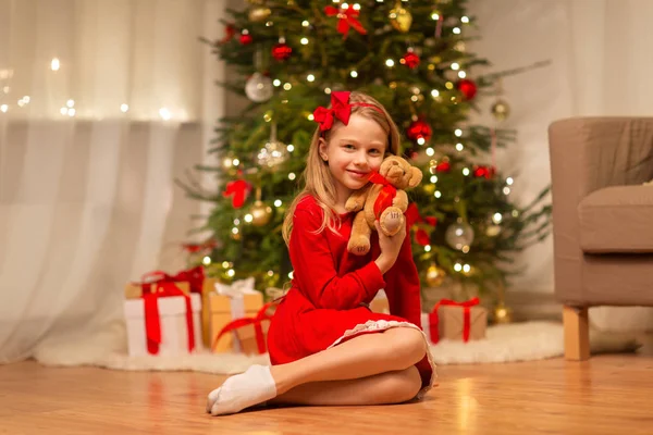Girl in red dress hugging teddy bear at home — Stock Photo, Image