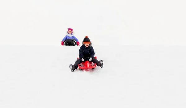 Szczęśliwy dzieci ślizgające się na sankach w dół wzgórza zimą — Zdjęcie stockowe