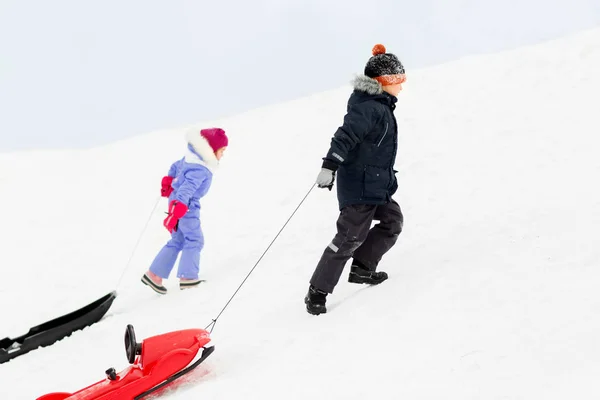 Barn med slädar klättring snow hill i vinter — Stockfoto