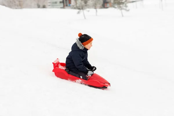 Щасливий хлопчик ковзає на санчатах сніговий пагорб взимку — стокове фото