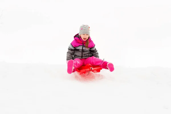 Gelukkig klein meisje glijden naar beneden op slee in de winter — Stockfoto