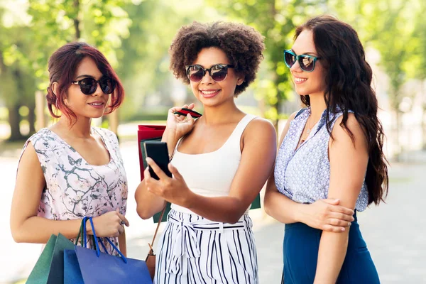 Mulheres com smartphones e sacos de compras na cidade — Fotografia de Stock