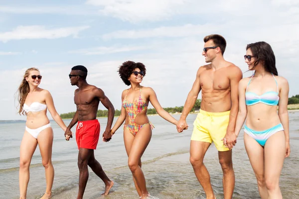 Šťastní přátelé kráčející podél letní pláže — Stock fotografie
