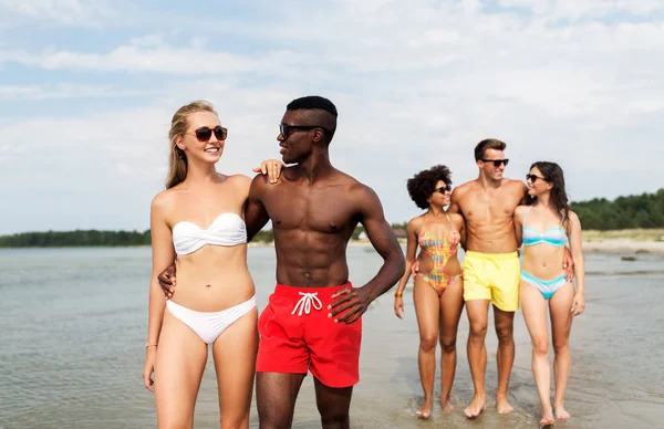 Gemengd ras paar wandelen langs het strand met vrienden — Stockfoto