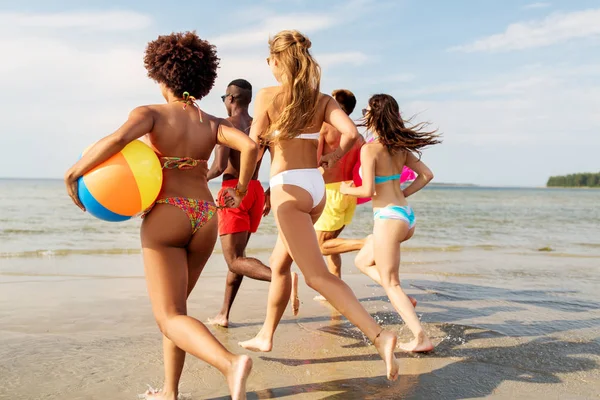 Φίλοι τρέχουν με μπάλα παραλία και στρώμα κολύμβησης — Φωτογραφία Αρχείου