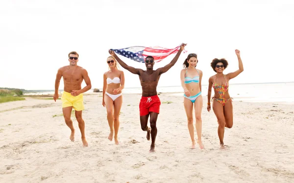 Amis heureux avec drapeau américain sur la plage d'été — Photo