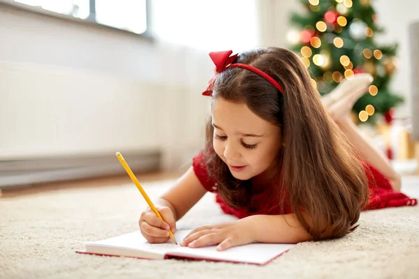 自宅でクリスマスの買い物リストを書く女の子 — ストック写真