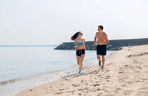 Casal em roupas esportivas correndo ao longo da praia — Fotografia de Stock