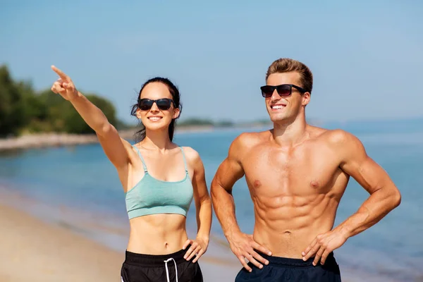 Šťastný pár v sportovní oblečení a odstíny na pláži — Stock fotografie