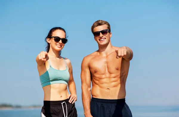 Lyckliga par i sportkläder och nyanser på stranden — Stockfoto