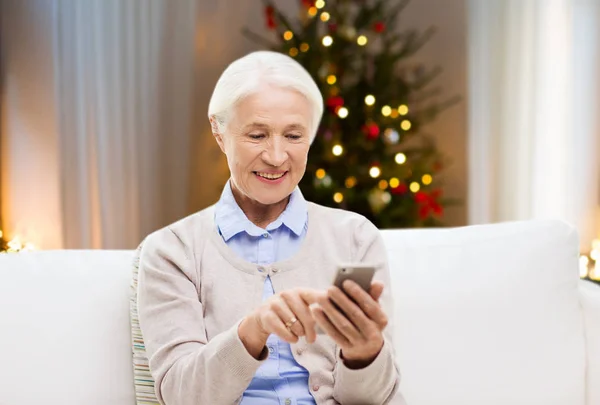 Senior vrouw met smartphone thuis op Kerstmis — Stockfoto