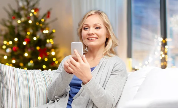 Женщина со смартфоном дома на Рождество — стоковое фото