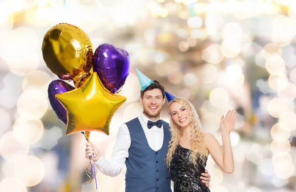 Casal feliz com tampas de festa e balões — Fotografia de Stock