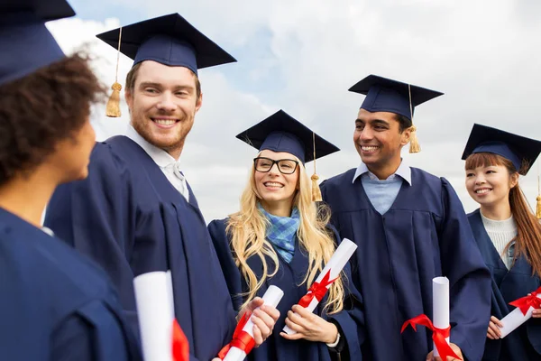 Šťastní studenti v minometných tabulích s diplomy — Stock fotografie