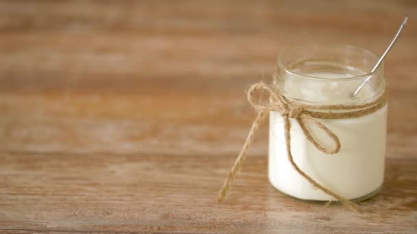 Йогурт или сметана в стеклянной банке на деревянном столе — стоковое видео